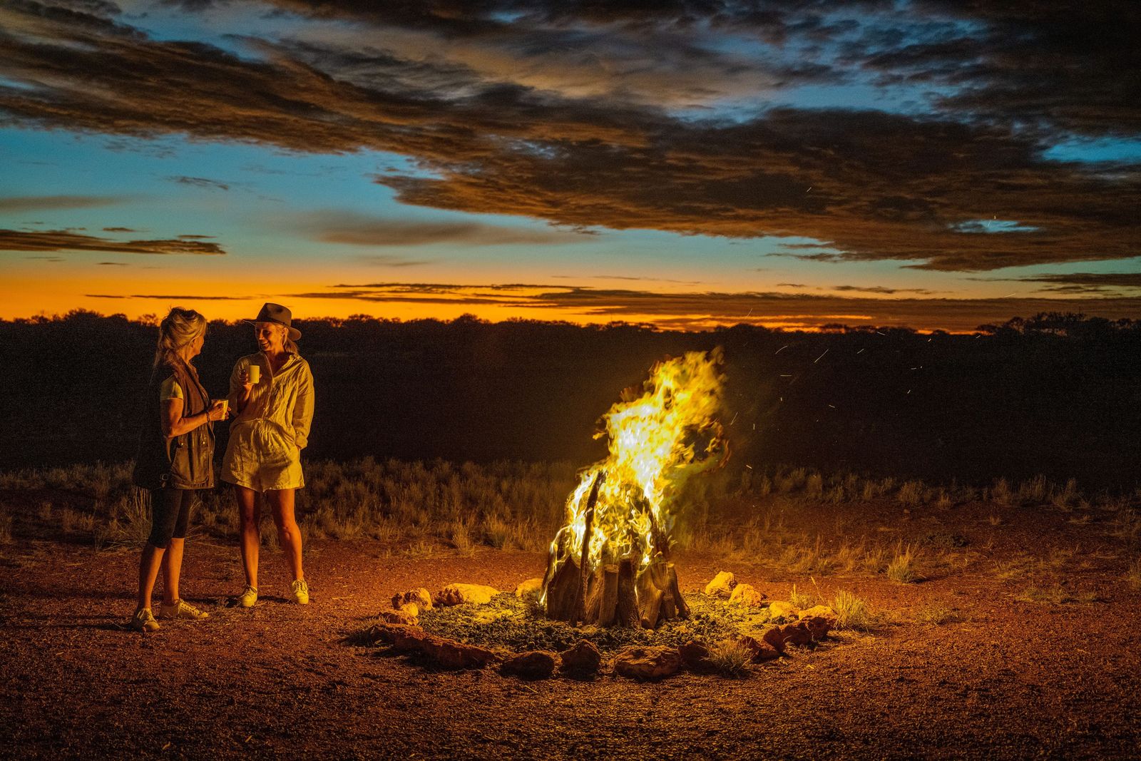 Guests beside a campfire under an outback sunset during a Ghan stop. Photo: Tourism Australia