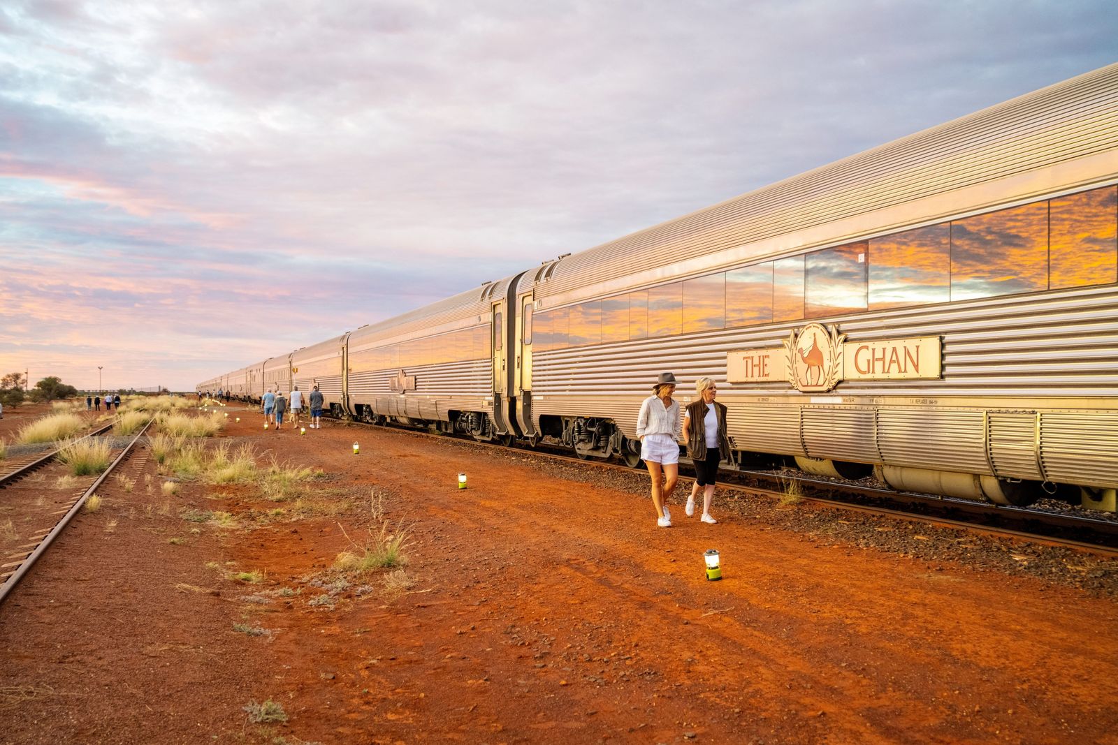 Guests walking beside The Ghan on red outback earth at sunset
