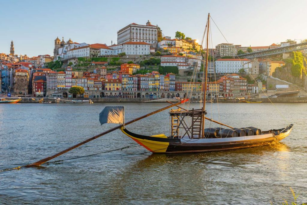Traditional rabelo boat on the Douro River in Porto, Portugal, with colorful buildings and a bridge in the background.