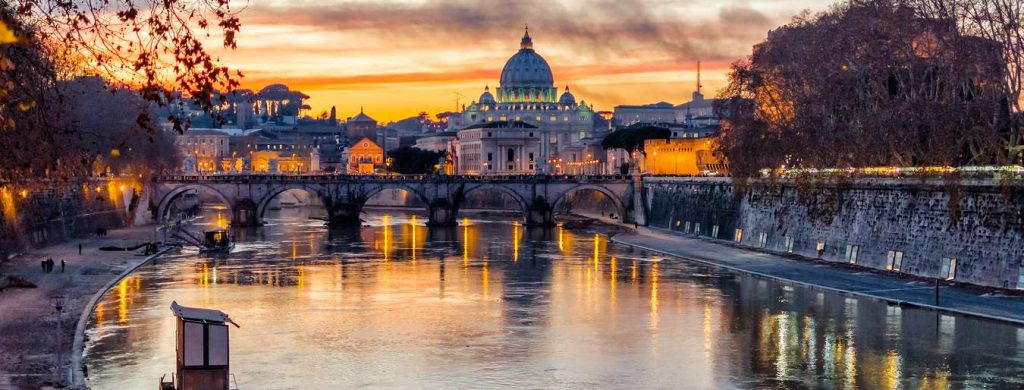Sunset view of St. Peter's Basilica over the Tiber River in Rome, Italy. Golden light reflects on the water.