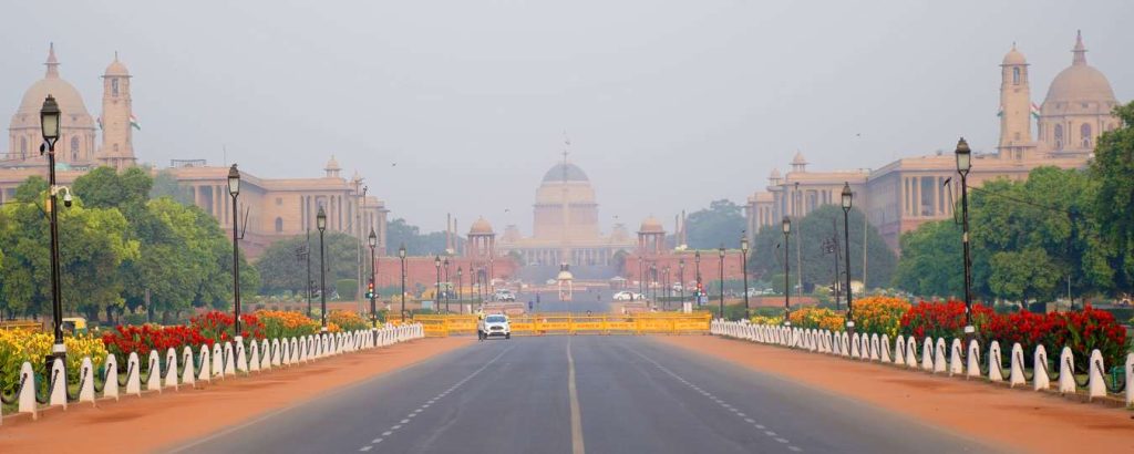 Wide view of Rashtrapati Bhavan in New Delhi, India, with road, flowers, and lamp posts.