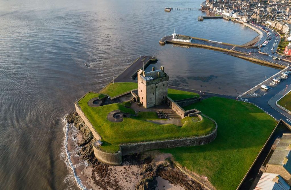 Aerial view of Broughty Castle, a stone fortress on Scotland's coast, surrounded by green grass and the sea.