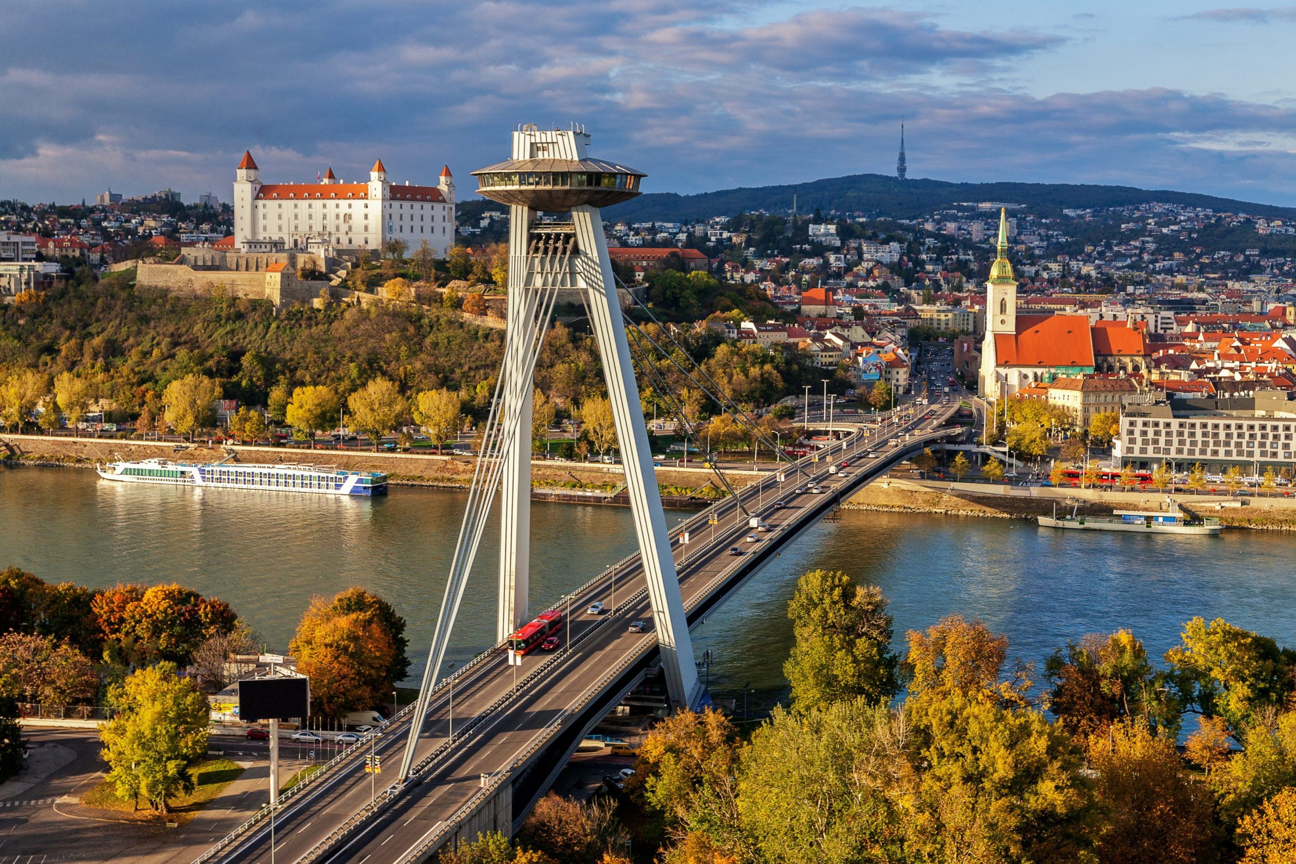 Bratislava cityscape featuring the UFO bridge over the Danube River, Bratislava Castle, and colorful autumn trees.
