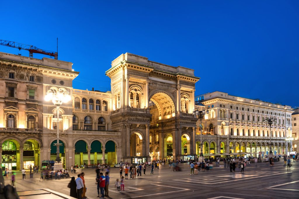 People walking near Vittorio Emanuele II gallery at Duomo square, Milan, Italy. Night view of street and buildings