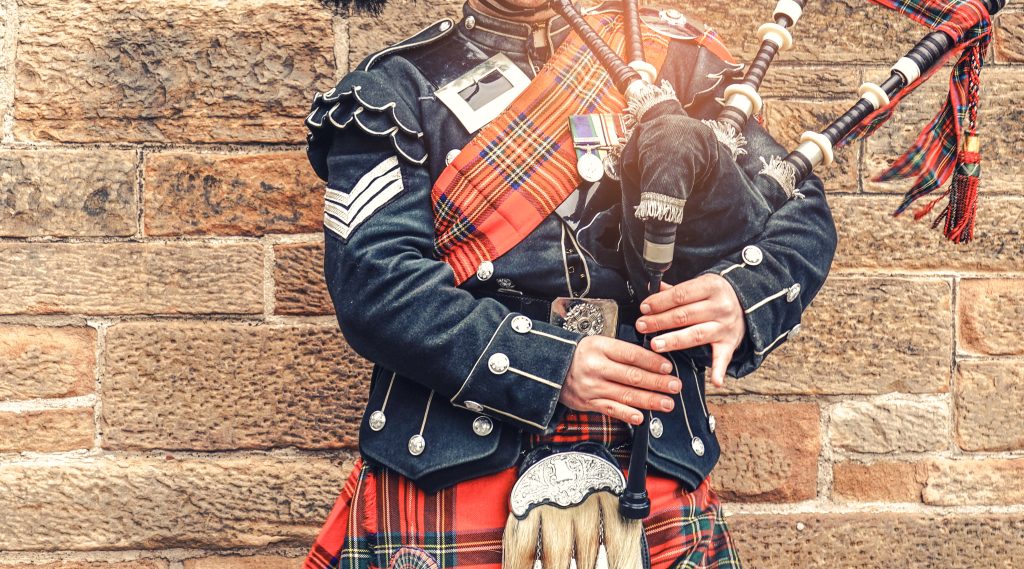 EDINBURGH, SCOTLAND, 24 March 2018, Scottish bagpiper dressed in traditional red and black tartan dress stand before stone wall. Edinburgh, the most popular tourist city destination in Scotland.