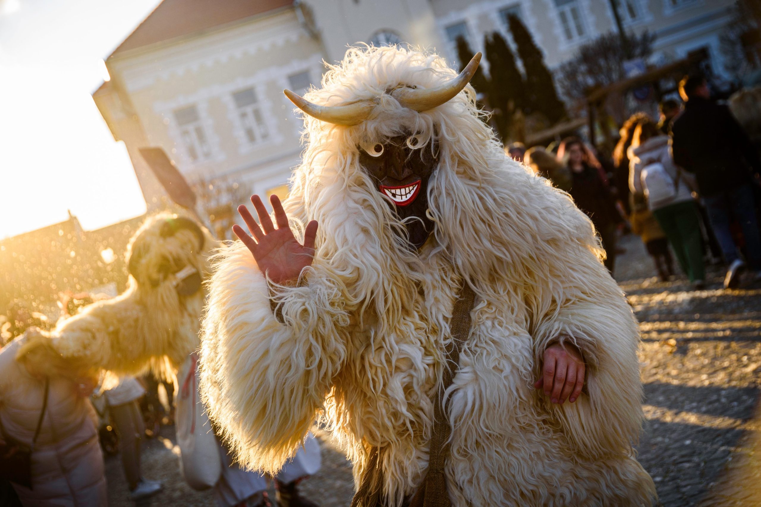 A person in a furry white costume with horns and a black mask waves during the Busójárás festival in Mohács, Hungary.