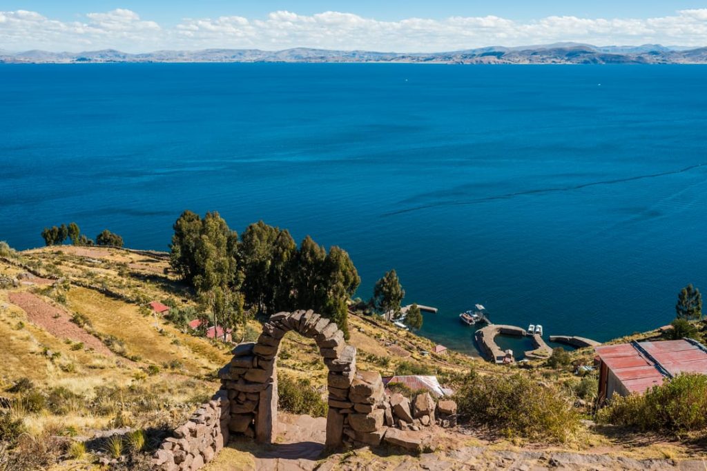 Scenic view of Lake Titicaca, Peru, with a stone archway framing the blue waters and distant mountains, showcasing island life.