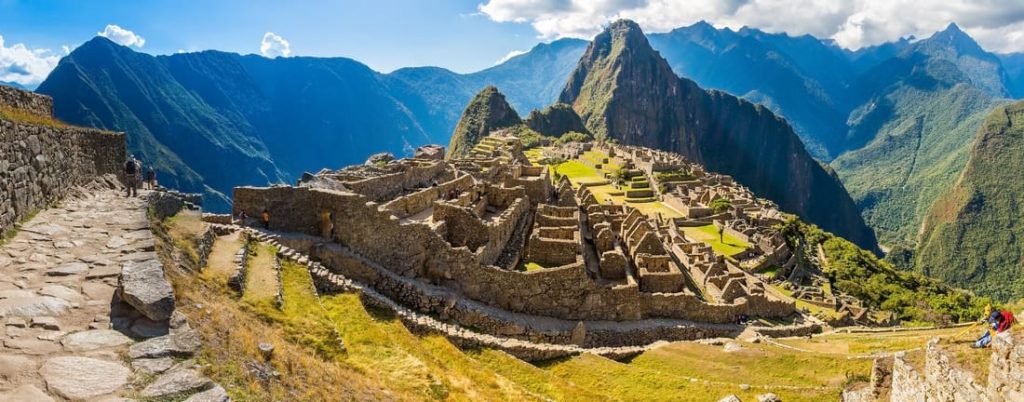 Panoramic view of Machu Picchu, the ancient Inca citadel in Peru, showcasing stone structures, terraces, and surrounding mountains under a blue sky.