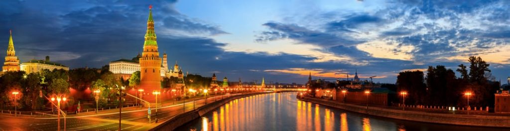 Panoramic view of the Moscow Kremlin and Moskva River at dusk, with illuminated buildings and reflections on the water.