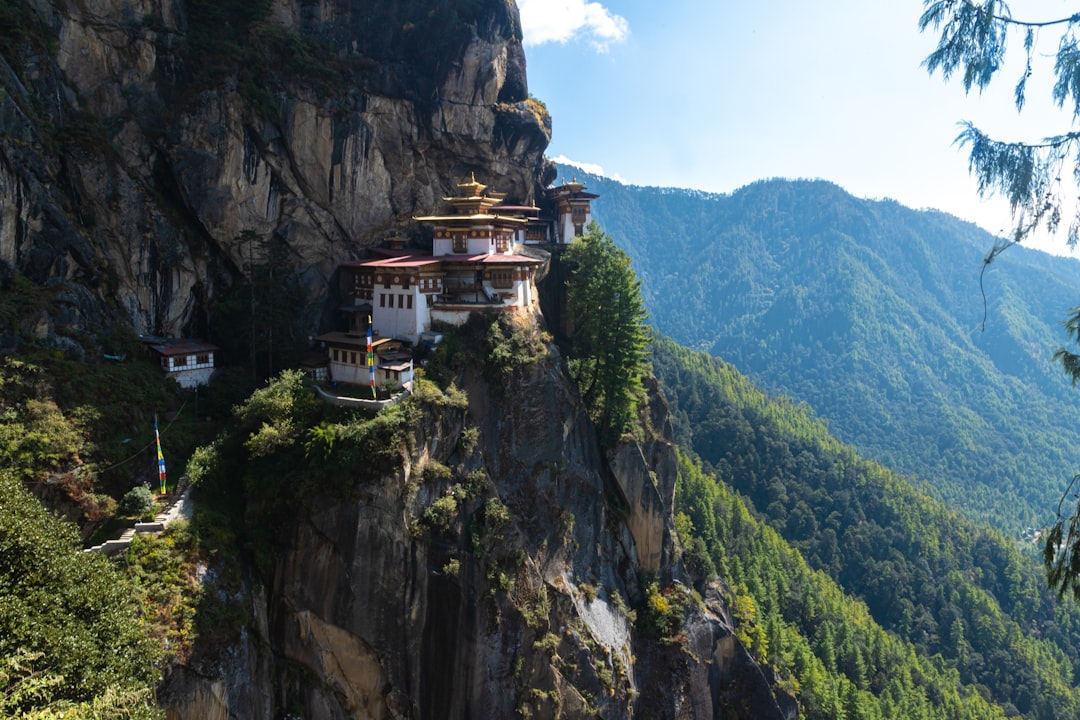 The Tiger's Nest Monastery clings to a steep cliffside in Bhutan, with green mountains in the background.