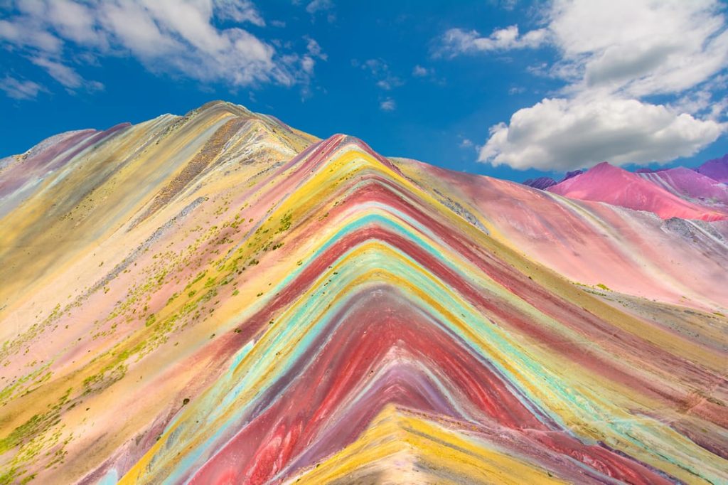 Colorful Rainbow Mountain in Peru, showcasing vibrant geological layers under a blue sky with scattered clouds. A stunning Andean landscape.