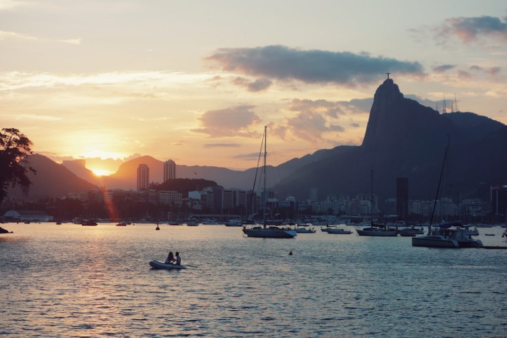 Sunset over Guanabara Bay, Rio de Janeiro, with Christ the Redeemer statue atop Corcovado Mountain. Two people in a small boat.