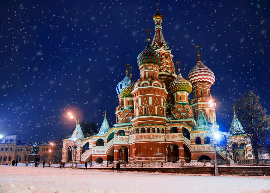 St. Basil's Cathedral in Moscow, Russia, stands majestically under a snowy night sky. Ornate domes and colorful architecture are illuminated.
