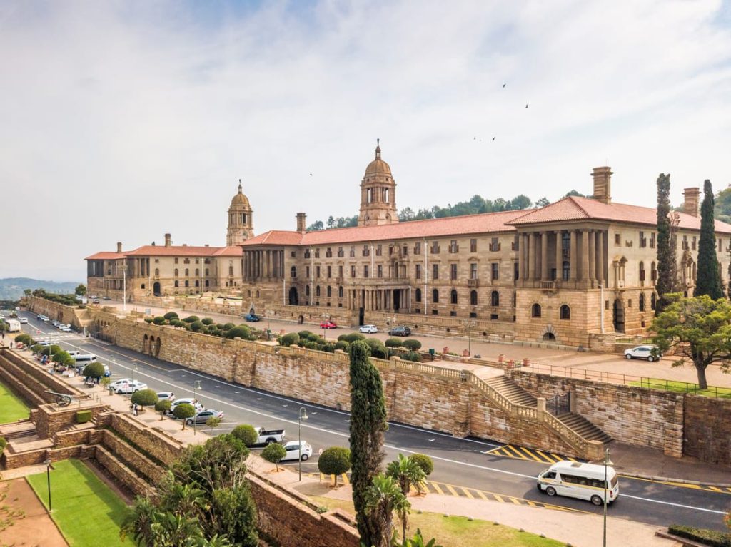 The Union Buildings in Pretoria, South Africa, a large sandstone building complex with towers, gardens, and a road in front.