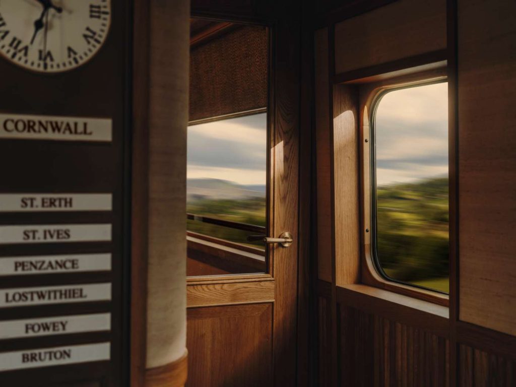 Interior of a vintage train car featuring wood paneling, destination signs, and blurred countryside views through the window.