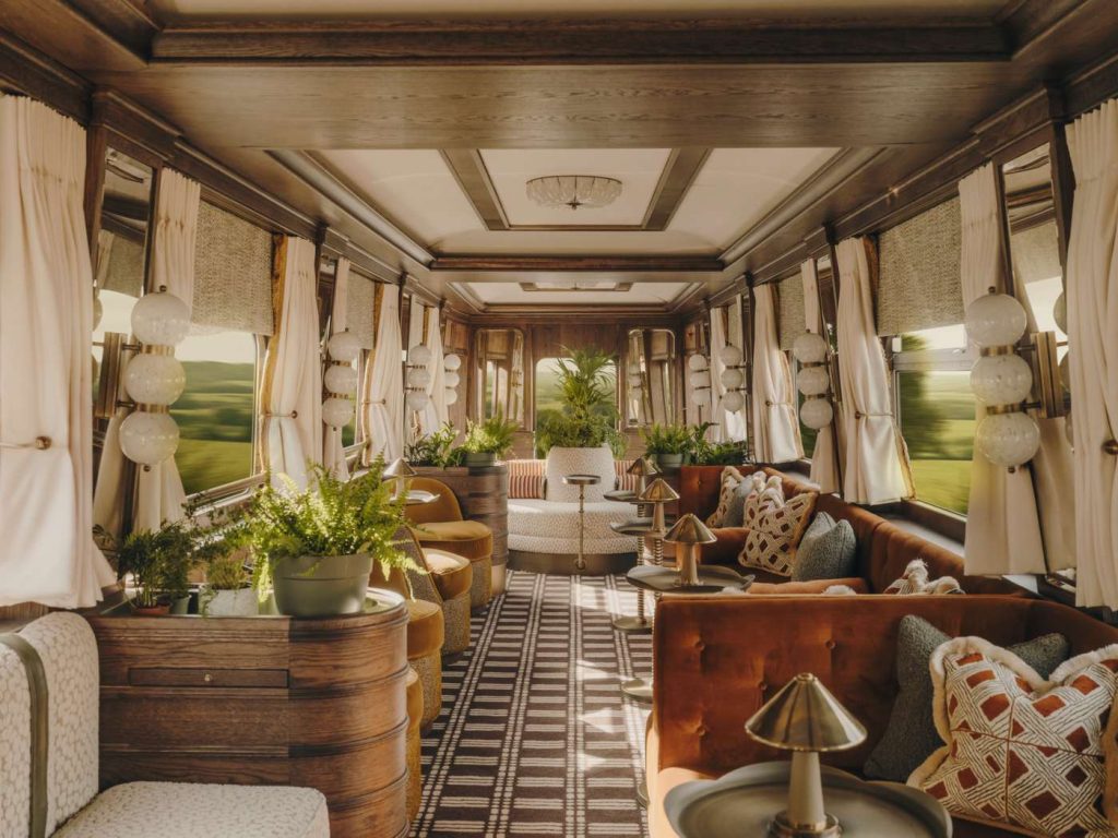 Ornate train car interior with plush seating, plants, and views of passing landscape. Warm, inviting, and luxurious.