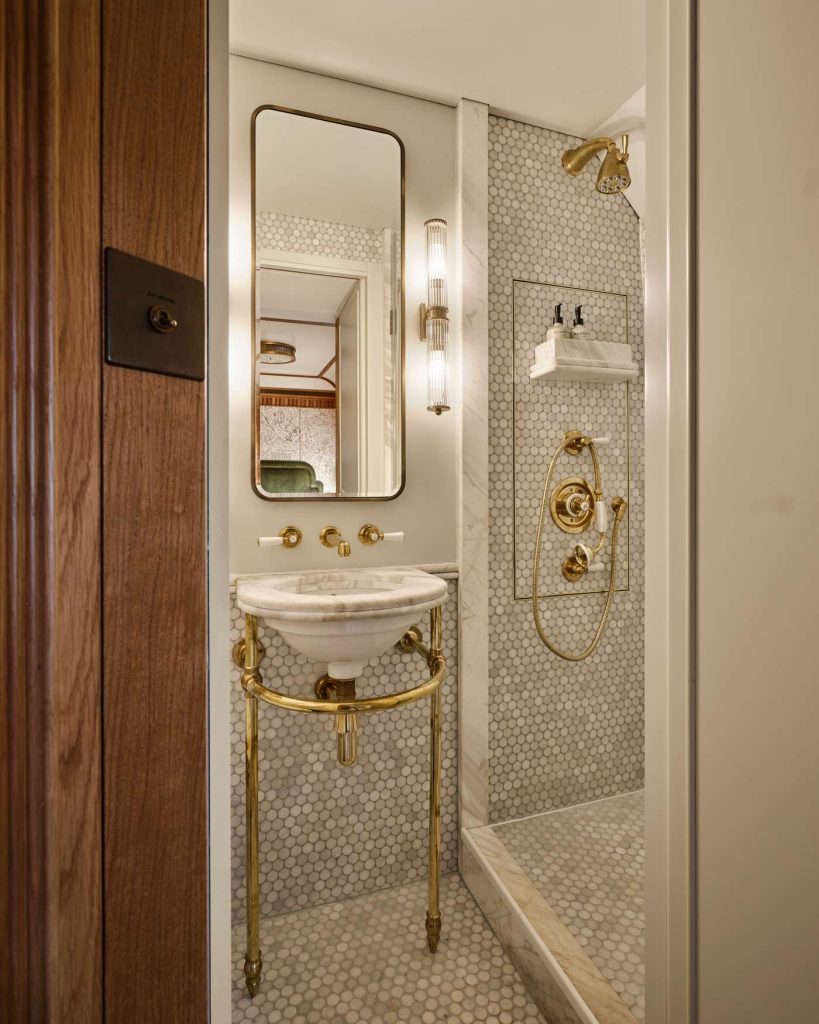 A small bathroom features marble mosaic tiles, gold fixtures, and a vintage-style sink and shower.