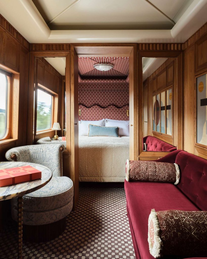Ornate train cabin features a bedroom, lounge with red sofa, patterned floors, and wood paneled walls.