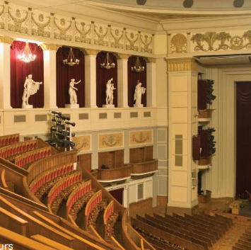 Ornate opera house interior featuring red velvet seating, statues, and gilded architectural details.