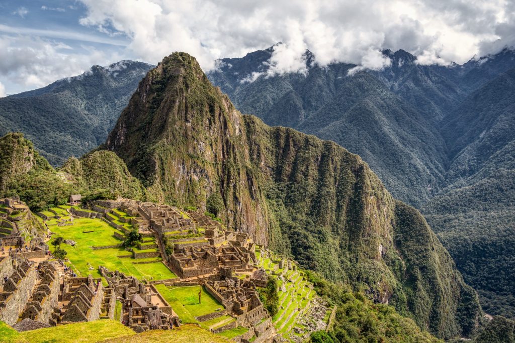 High angle view of Machu Picchu, an ancient stone city with green terraces, nestled in the Peruvian Andes mountains under a cloudy sky.