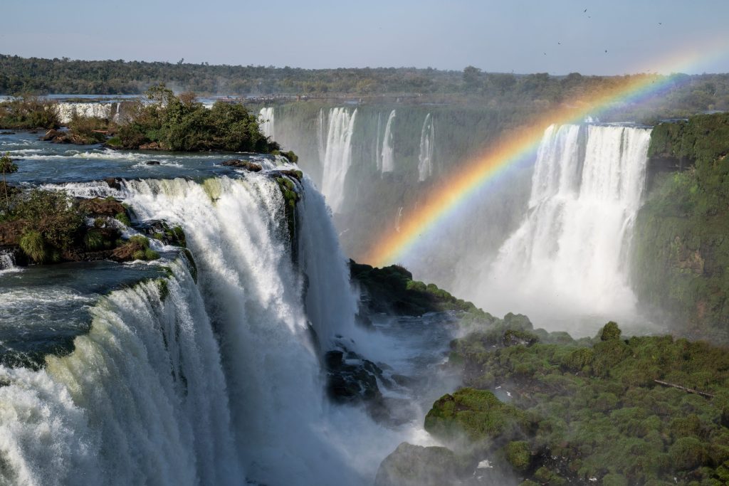 Breathtaking view of Iguazu Falls with a vibrant rainbow arcing across the cascading water and lush greenery.