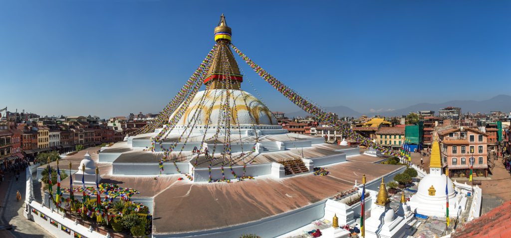 Boudhanath Stupa in Kathmandu, Nepal, a large white dome with golden spire, prayer flags, and surrounding buildings.