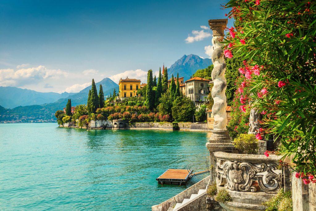 Scenic Lake Como view with Italian villas, lush gardens, mountains, and turquoise water.