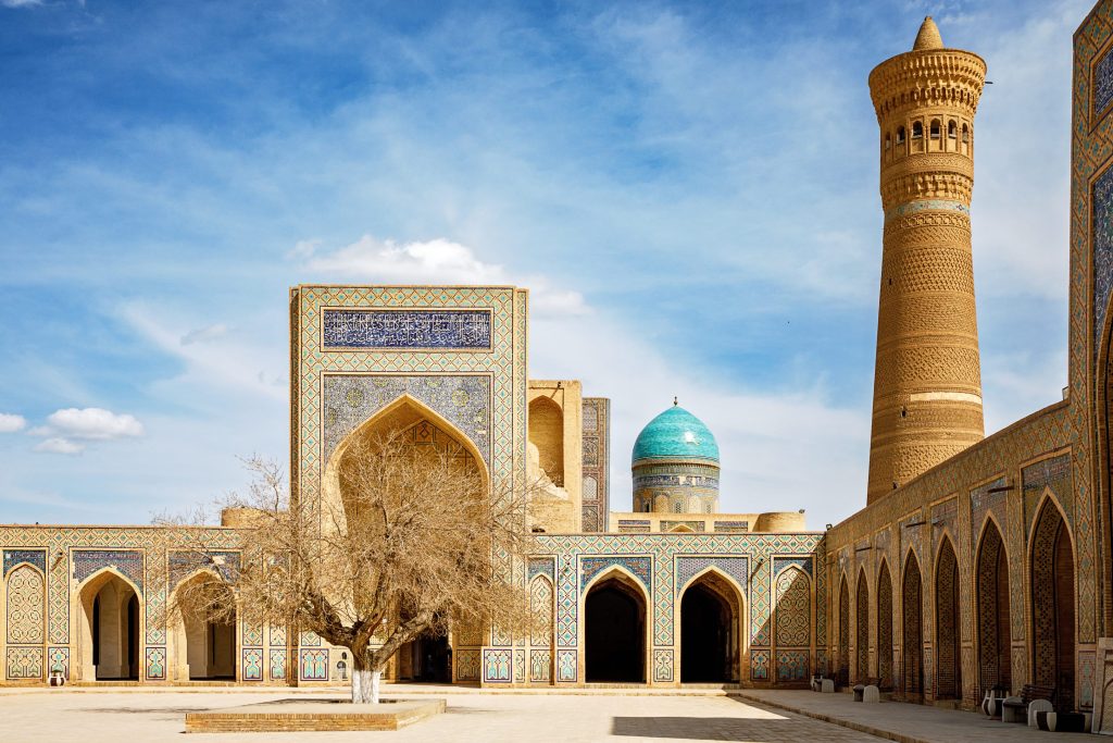 Courtyard view of Kalyan Minaret and Mir-i-Arab Madrasah in Bukhara, Uzbekistan, with intricate tilework and blue dome.