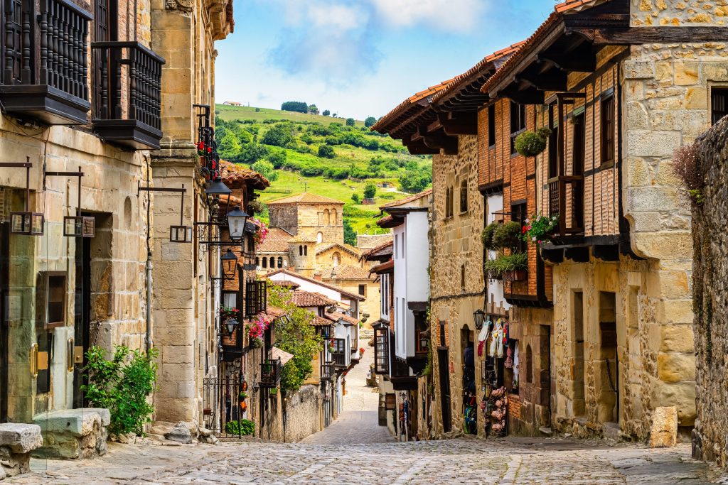 Cobblestone street winds through Santillana del Mar, Spain, lined with historic stone buildings and balconies with flowers.