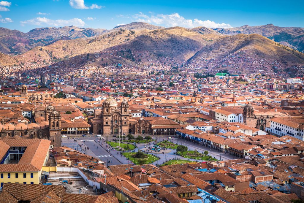 Aerial view of Cusco, Peru, featuring red tile roofs, Plaza de Armas, and distant mountains.