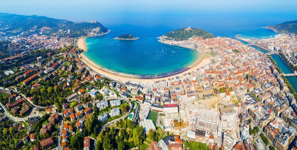 Aerial view of San Sebastian, Spain featuring La Concha beach, blue water, and colorful buildings.