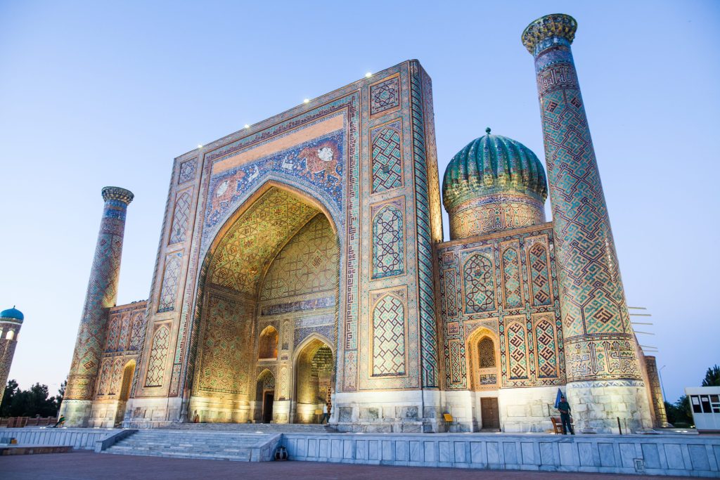 The Registan Square in Samarkand, Uzbekistan features ornate Islamic architecture, minarets, and intricate tilework under a twilight sky.