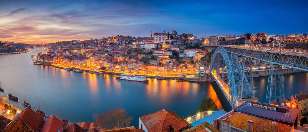 Porto, Portugal cityscape at dusk with Dom Luís I Bridge spanning the Douro River, lights reflecting on the water.