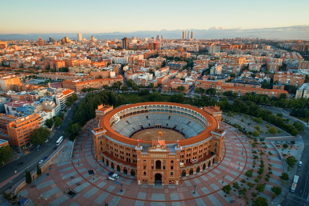 Aerial view of Las Ventas bullring in Madrid, Spain, surrounded by cityscape, under a bright sky.