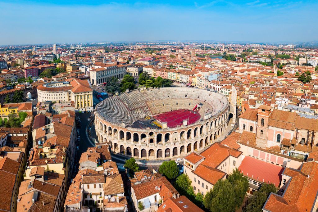 Aerial view of Verona, Italy, featuring the ancient Roman Arena, surrounded by buildings with red tile roofs.