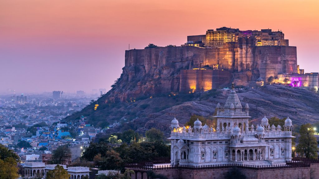 Jodhpur's Mehrangarh Fort atop a hill overlooks the white Jaswant Thada mausoleum during a colorful sunset.