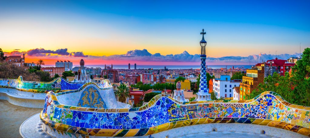 Panoramic view of Park Güell in Barcelona, featuring colorful mosaic benches overlooking the city at sunset.
