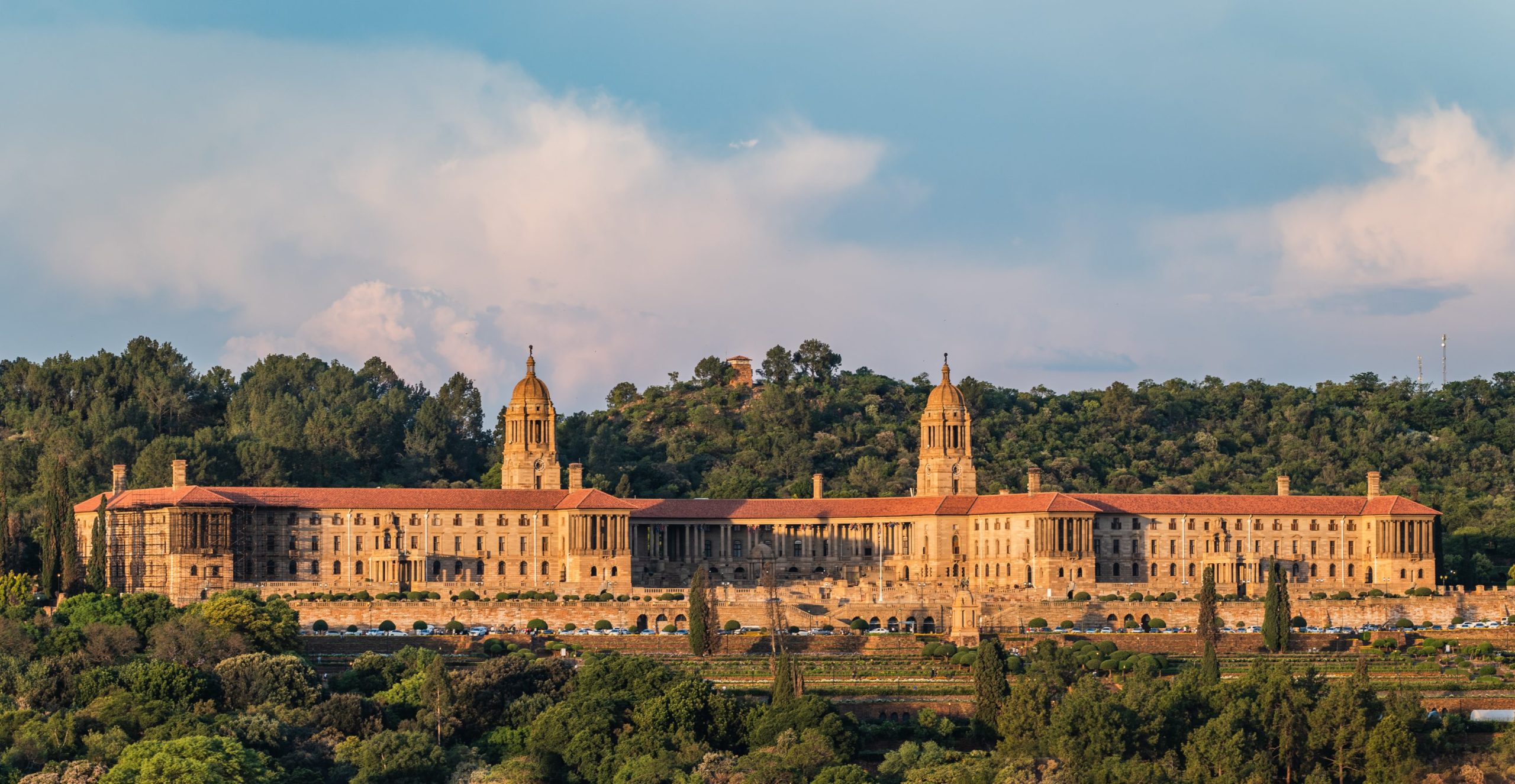 Wide shot shows the Union Buildings in Pretoria, South Africa. The large sandstone building sits atop a green hill.