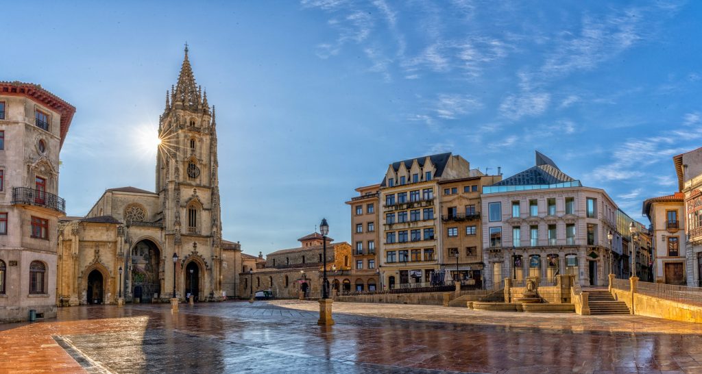 Wide shot of Oviedo's Plaza del Ayuntamiento, featuring the Cathedral, historic buildings, and wet cobblestones.