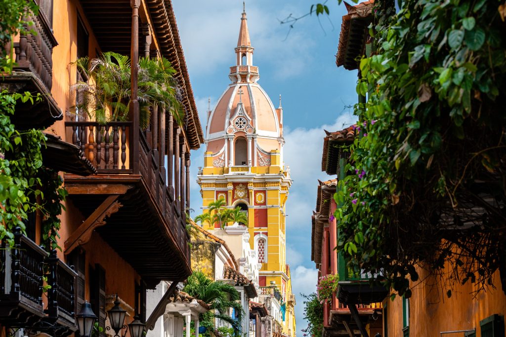 Colorful buildings and a church tower in Cartagena, Colombia, with balconies and lush greenery.