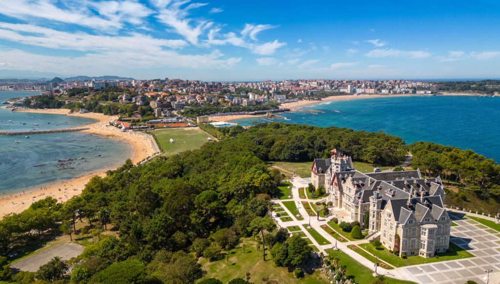 Aerial view of Magdalena Palace, Santander, Spain, with beaches, green peninsula, blue ocean, and city skyline.