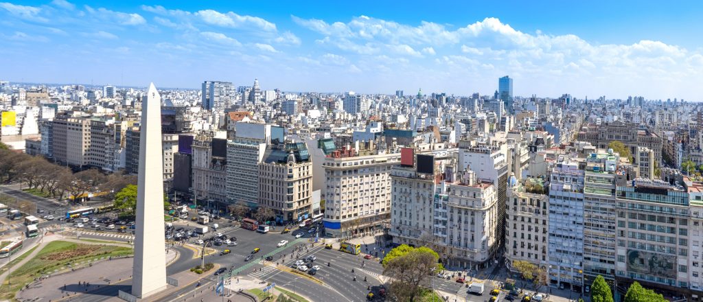 Panoramic view of Buenos Aires, Argentina, featuring the Obelisco monument and dense urban cityscape under a blue sky.