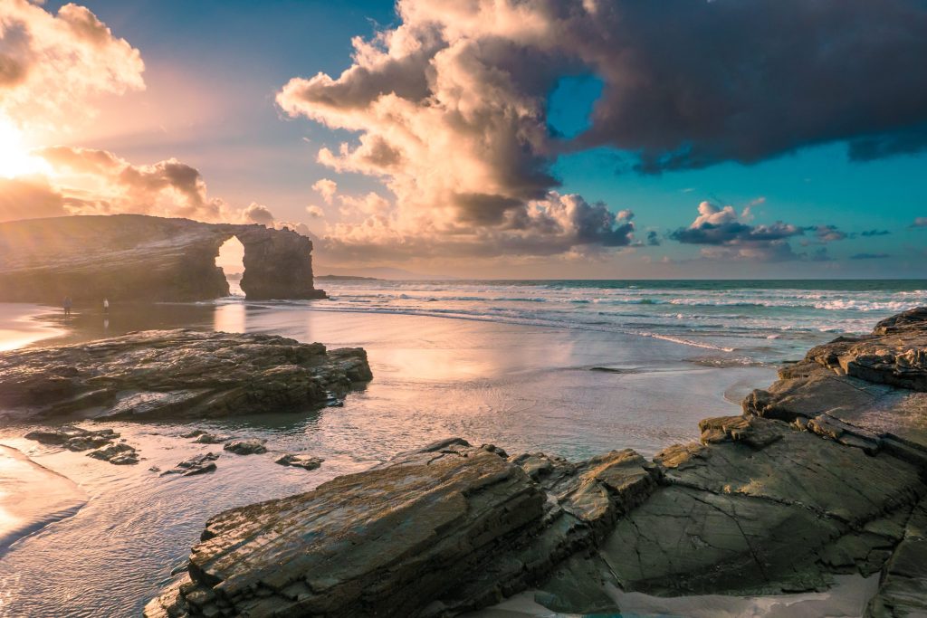 Scenic view of As Catedrais beach in Ribadeo, Spain at sunset with rock formations and colorful sky.