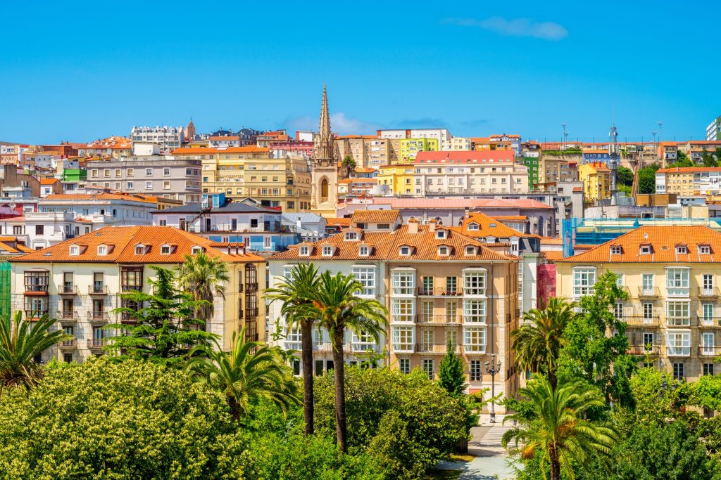 Colorful buildings and palm trees in Oviedo, Spain under a clear blue sky.