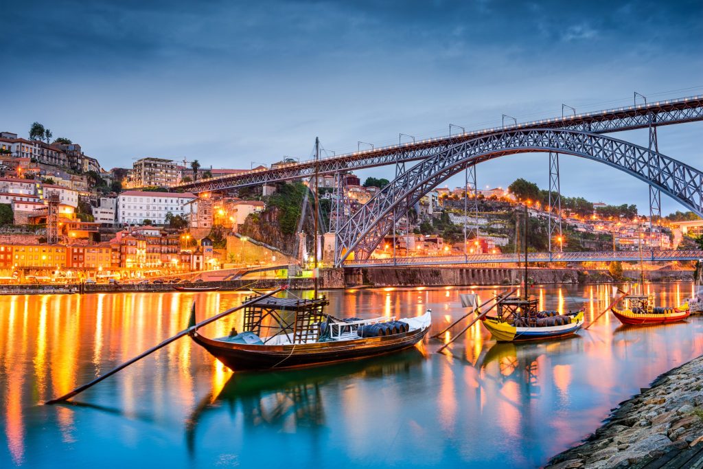 Evening view of Porto, Portugal, featuring the Douro River, Dom Luís I Bridge, and colorful boats.