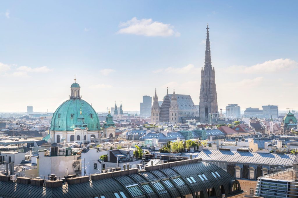 Panoramic view of Vienna, Austria featuring St. Stephen's Cathedral, green dome, and cityscape under a bright sky.