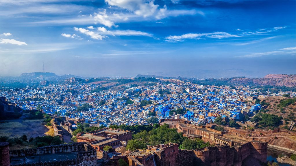 Panoramic view of Jodhpur, India, showcasing blue buildings under a bright blue sky with white clouds.