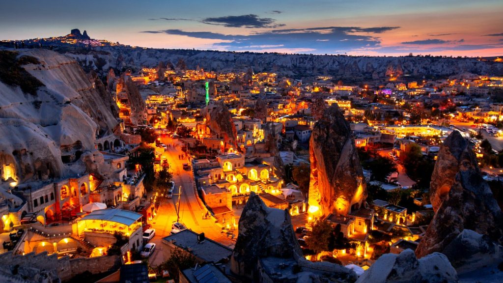 The cave town of Goreme in Cappadocia, Turkey, lit up at dusk beneath its rock formations.