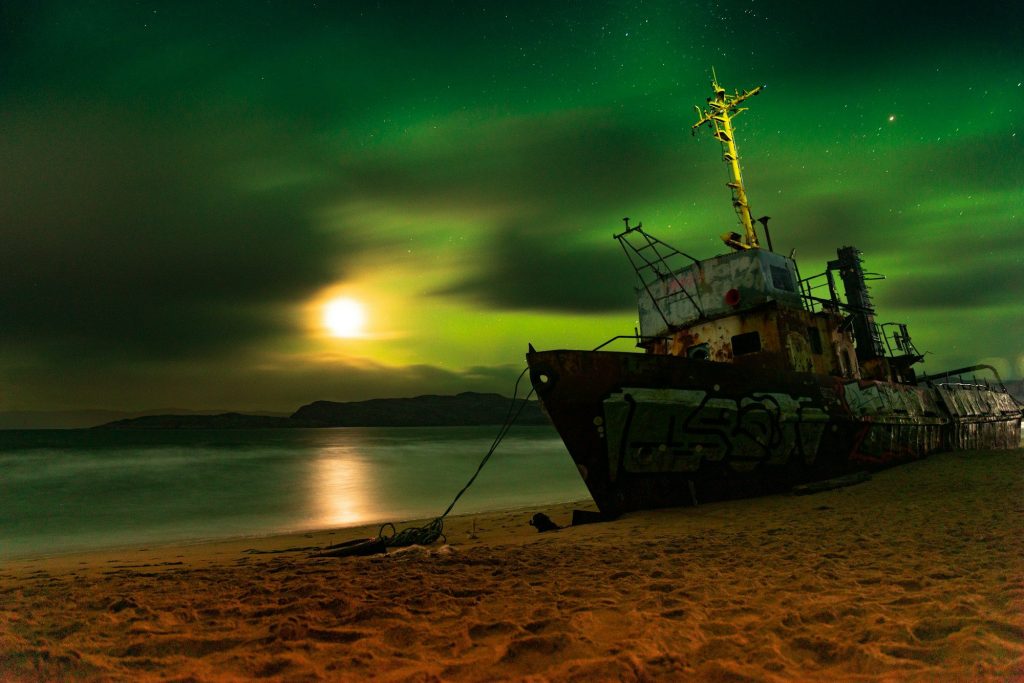 A boat on the Barents Sea shore under the northern lights — Teriberka, Murmansk Oblast, Russia