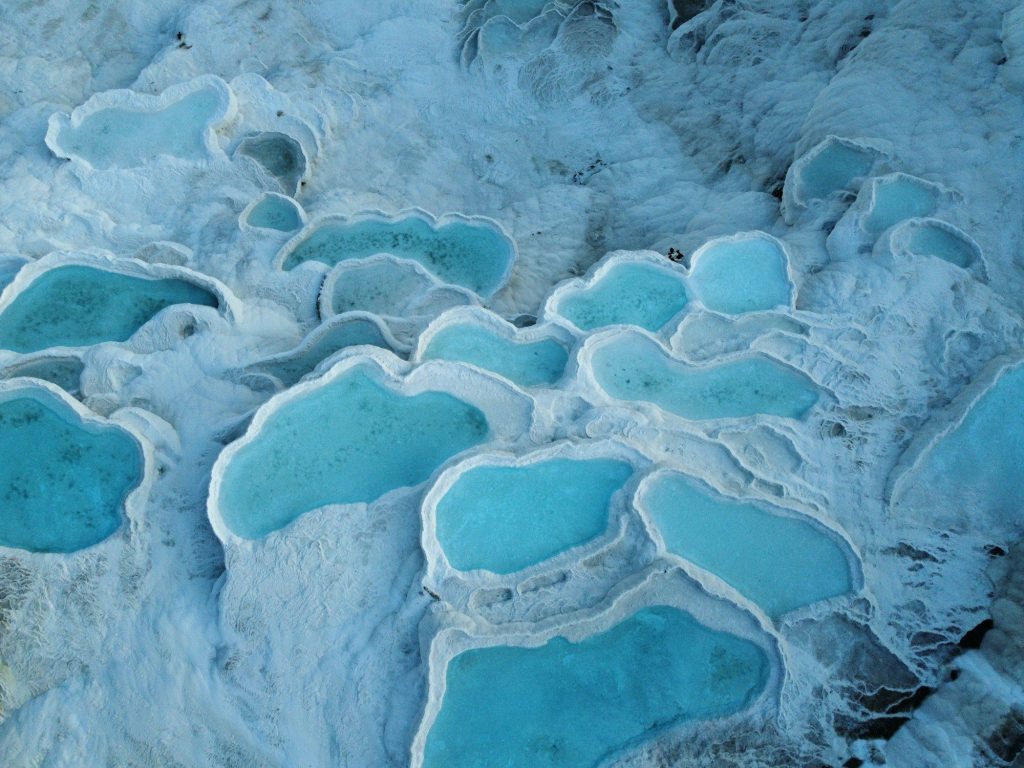 White travertine terraces and turquoise thermal pools at Pamukkale, beside the ruins of Hierapolis near Denizli, Turkey.